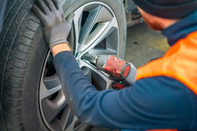 Close-up shot of a modern car's front suspension system featuring a silver upper control arm, coilover shock absorber, brake rotor, and steering rack components.